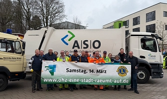 Die Initiatoren der Aktion stehen hinter einem Banner mit dem Datum der Veranstaltung vor einem Müllfahrzeug von der ASO.